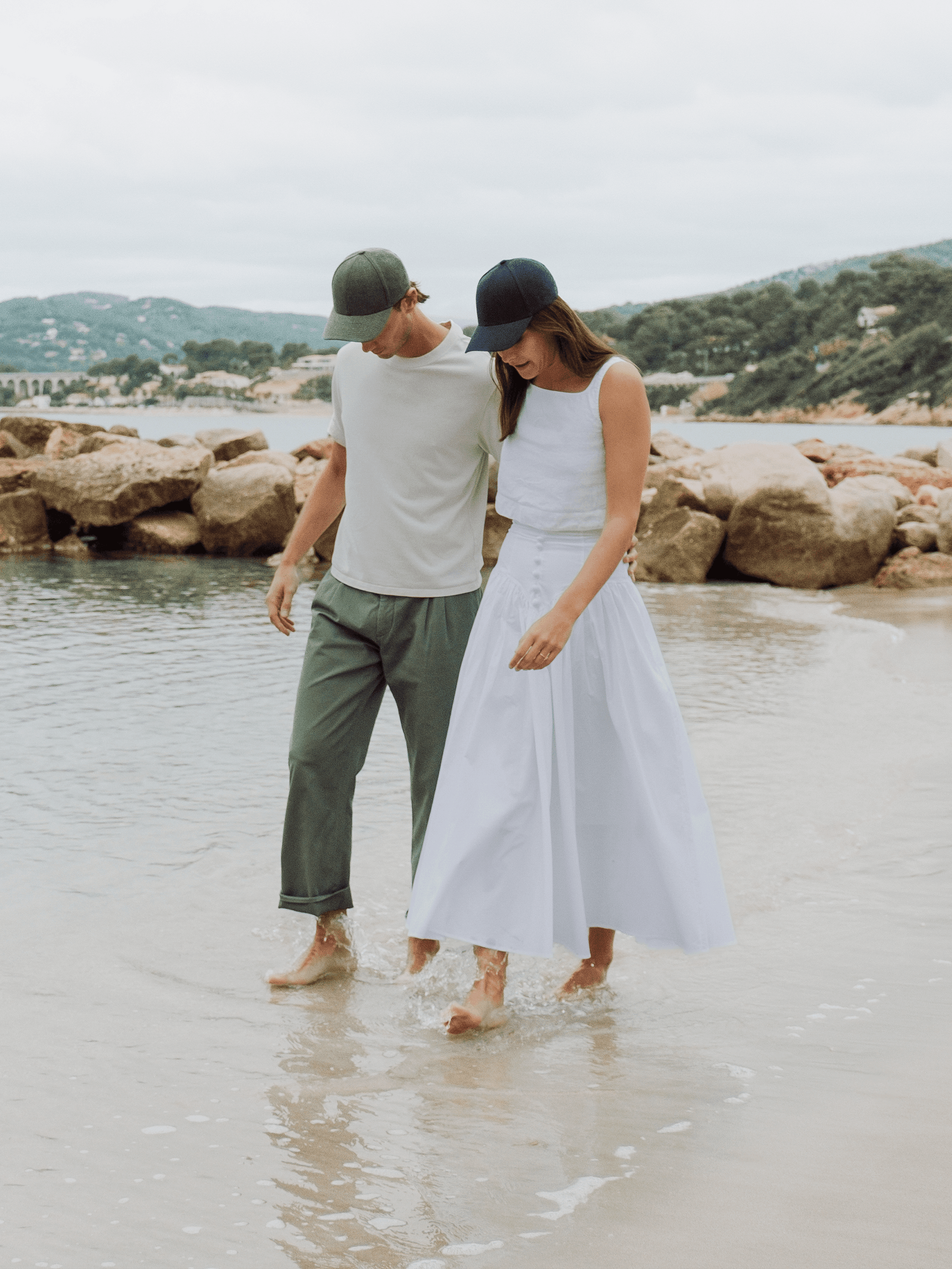 Front view of female and male model wearing green and dark navy linen cap on beach